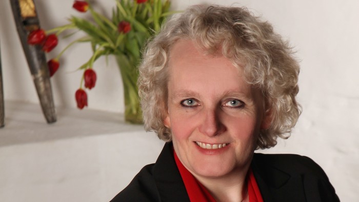 Frau mit blondem Haar und roter Bluse sitzt vor Blumenstrauß