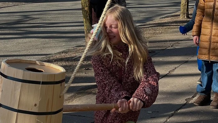 Et barn svinger på et bildæks-sving i det fri med tilskuere i baggrunden.