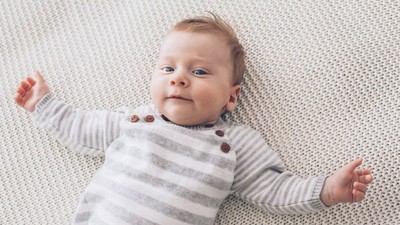 Et spæd barn ligger på ryggen på et hvidt og gråt farvet madrassel.