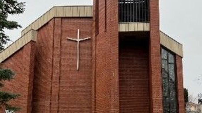 Das Bild zeigt eine moderne Ziegelkirche mit Kreuz und hohem Turm.