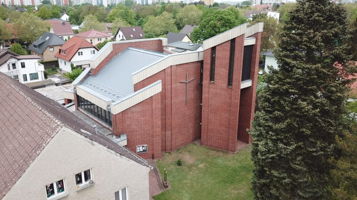 Ein modernes Kirchengebäude aus rotem Backstein in einem Wohngebiet mit umliegenden Häusern und Bäumen.
