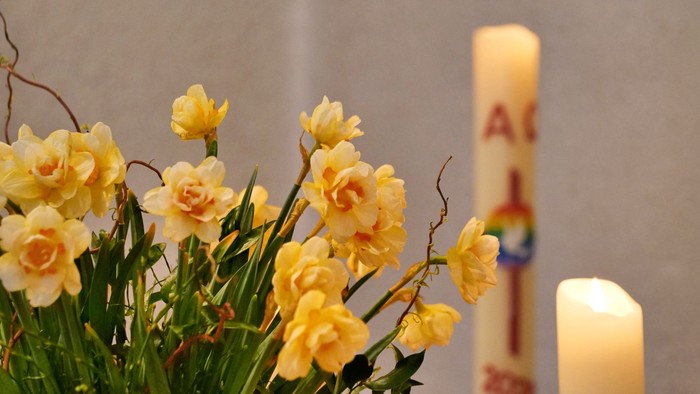 Gelbe Blumen und Kerzen vor weißer Wand