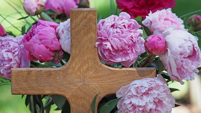 Elegante Holzkreuz, verziert mit lebendigen rosa-weißen Pfingstrosen in einer ruhigen Außenumgebung.