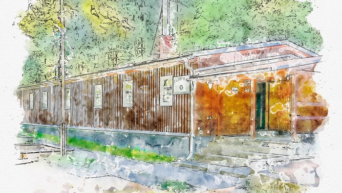 Ein altes, verwittertes Holzgebäude mit grünen Fensterläden und einer Uhr, umgeben von Bäumen und Grün.