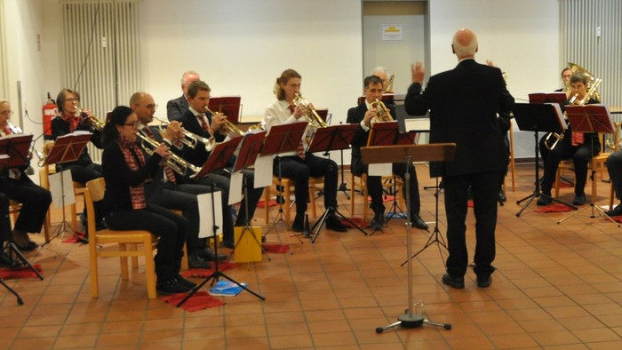 Eine Blaskapelle probt unter der Leitung eines Dirigenten in einem geräumigen Innenraum.