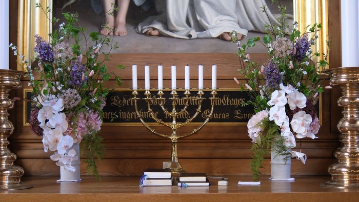 Elegant alter med religiøs kunst, blomsterdekorationer og en lysestage på træpanelering.