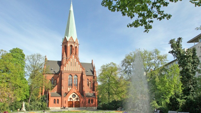 Ein rotes Kirche mit hohem Turm und ein Brunnen im Vordergrund