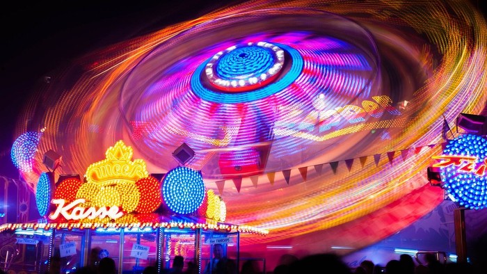 Leuchtende Achterbahn bei Nacht mit bunten Lichtern und Menschenmenge
