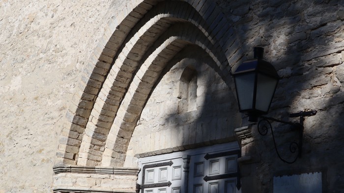 Steinbogen über einer Holztür mit wandmontierter Laterne.