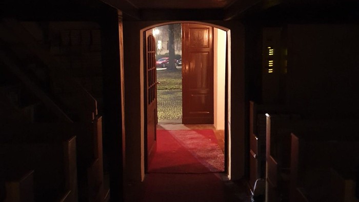 Dunkler Flur mit rotem Teppich, der zu offenen Holztüren führt.