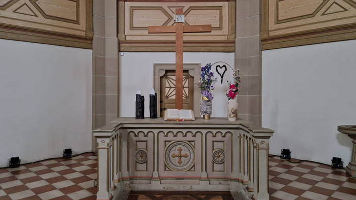 Das Bild zeigt einen Altar in einer Kirche mit Kreuz, Kerzen und Blumen.