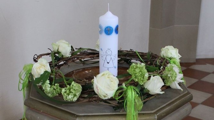 Ein kleiner Tisch mit weißer Kerze und grünen Blumen.