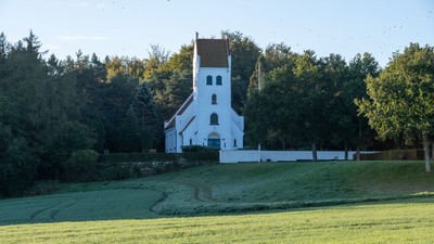 En hvid kirke med tårn og klokke i en grøn og træfattig omgivelse