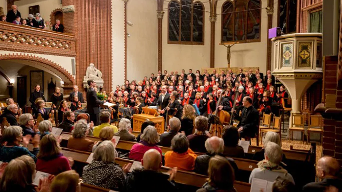 Eine große Kirchenversammlung mit vielen Menschen, die in Kirchenbänken sitzen und einem Chor zuhören.
