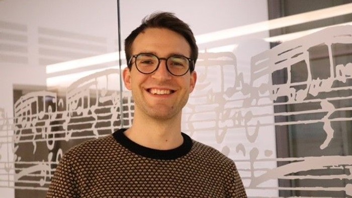 Junger Mann mit Brille vor weißem Hintergrund mit Skizzen.