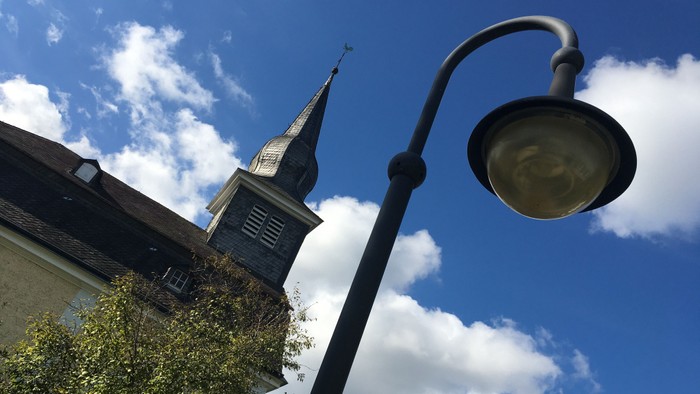 Ein Laternenpfahl vor einer Kirche mit hohem Turm und blauem Himmel.