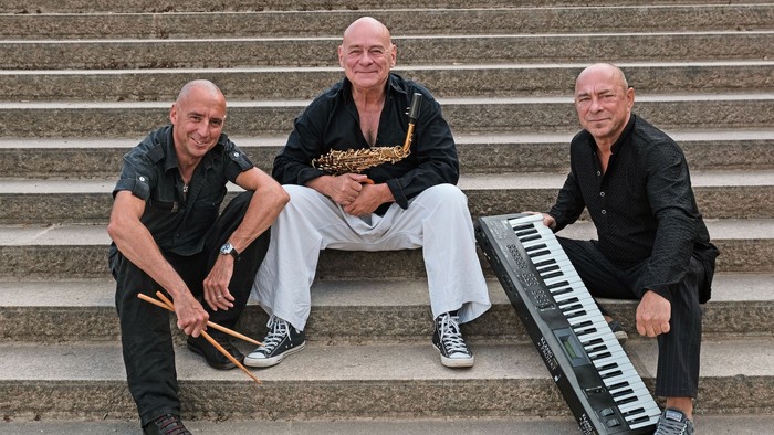Drei Musiker sitzen auf Treppenstufen, zwei mit Schlagzeug und Keyboard.