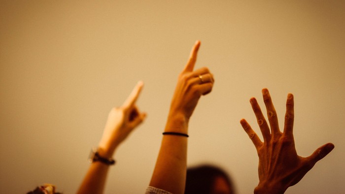 Drei Hände zeigen nach oben, eine mit Armband.