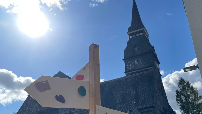 Bunter Holzschilderwald vor Kirche und modernem Gebäude