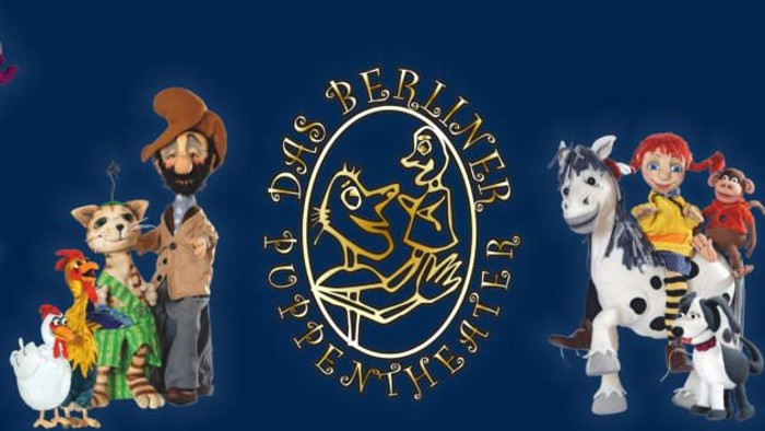Das Bild zeigt eine Puppenbühne mit verschiedenen Figuren und einem Logo in der Mitte.