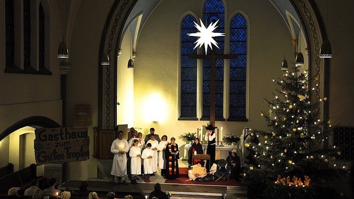 In der Kirche wird eine Weihnachtsfeier mit einem geschmückten Baum und einem Chor gefeiert.