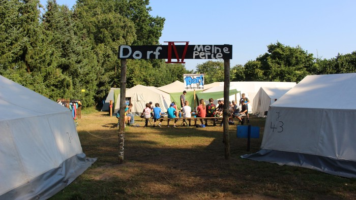 Ein Festivalgelände mit Zelten und Menschen unter Bäumen