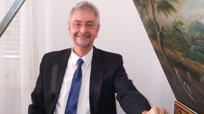 Mann in Anzug sitzt an einem Piano, vor einem Gemälde