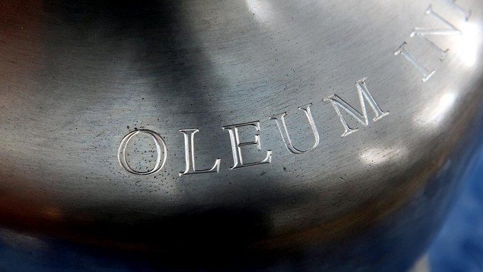 Nahaufnahme einer metallischen Oberfläche mit der eingravierten Aufschrift „OLEUM“ auf einem Behälterdeckel.
