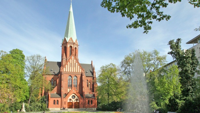 Ein rotes Kirche mit hohem Turm und ein Brunnen im Vordergrund