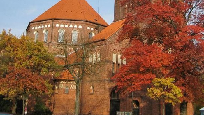 Ein rotes Backsteingebäude mit Uhrturm und Herbstlaub