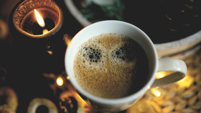 Eine Tasse Kaffee neben einer brennenden Kerze und Weihnachtsdekorationen