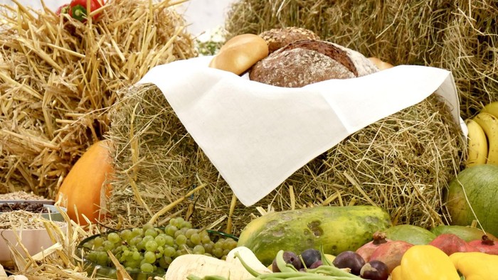Ernteprodukte wie Brot und Gemüse, zusammengestellt als Stilleben zu Erntedank, auf Strohballen