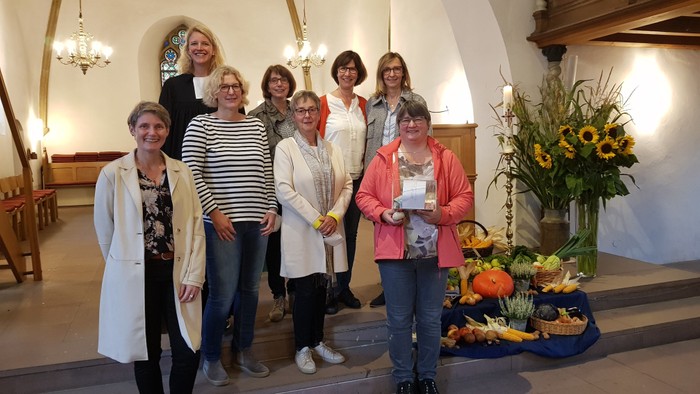 Eine Gruppe von Frauen steht in einer Kirche zusammen und hält einen Scheck sowie eine saisonale Obst- und Gemüseausstellung.