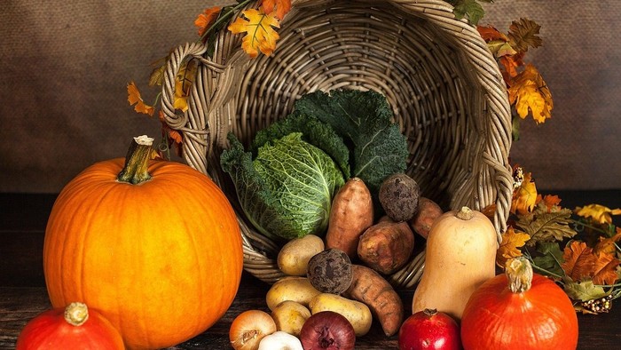 Ein Korb gefüllt mit Herbstgemüse und Kürbissen, umgeben von bunten Blättern