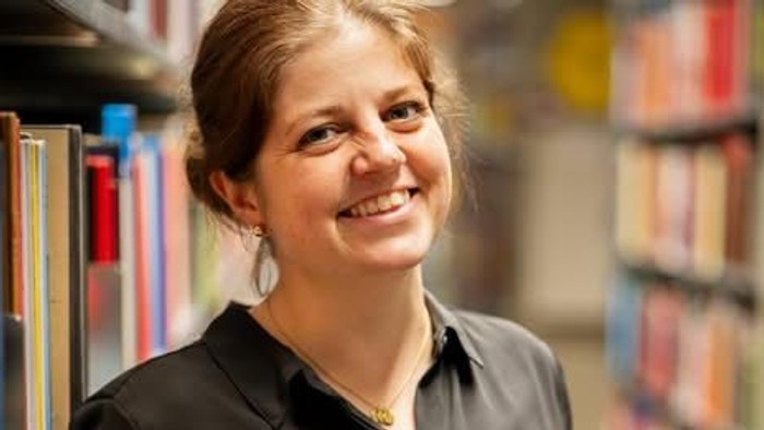 Line Bjerre står i en biblioteksafdeling med bøger.