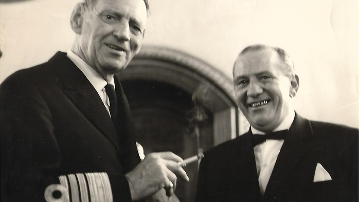 To mænd i jakkesæt giver hånd og smiler.