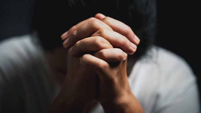 Person with hands clasped together, appearing in contemplation or prayer.