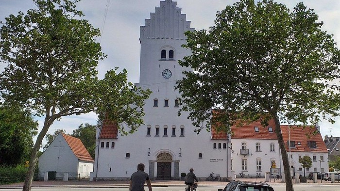 En hvid kirke med klokketårn og en gruppe mennesker foran