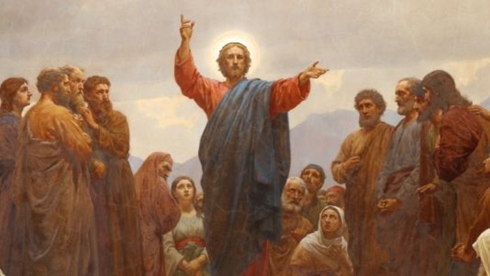 En mand i rød kappe taler til en folkemængde.