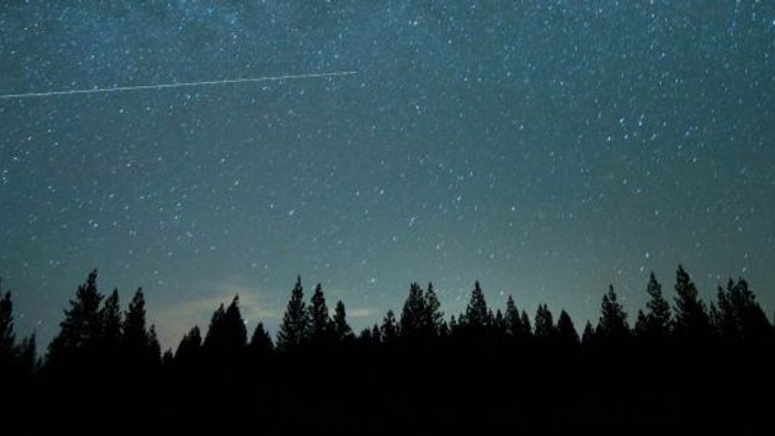 En stjerneskyer tager sin vej over et mørkt skovområde under et stjerneskud.
