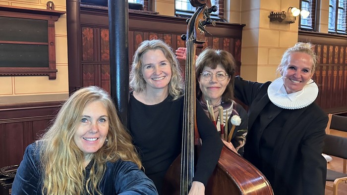 Fire musikere poser sammen i et stort rum med en cello mellem sig.