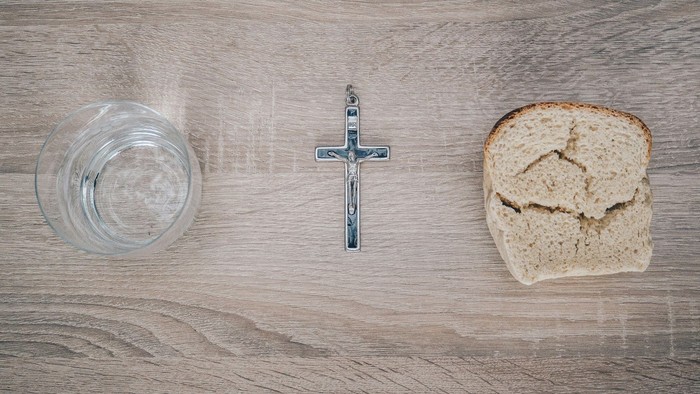 Enkel nadveropsætning med brød, et korsvedhæng og et glas vand på en træoverflade.