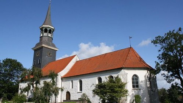 Weiße Kirche mit hohem Turm und rotem Dach auf grünem Rasen.