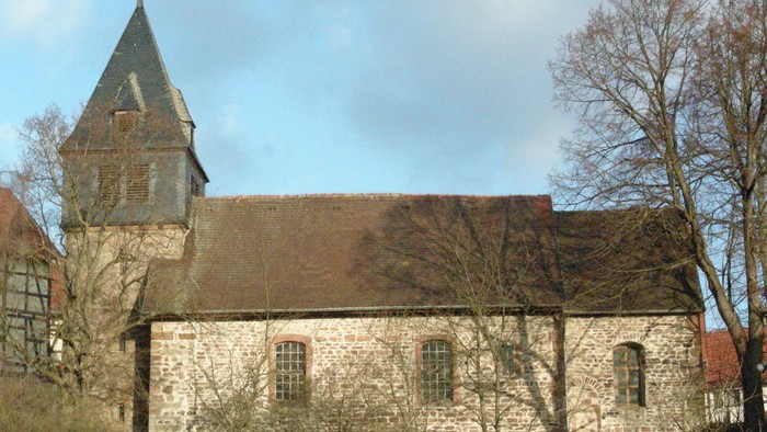 Alte Kirche mit Turm und spitzem Dach, umgeben von Bäumen und Büschen