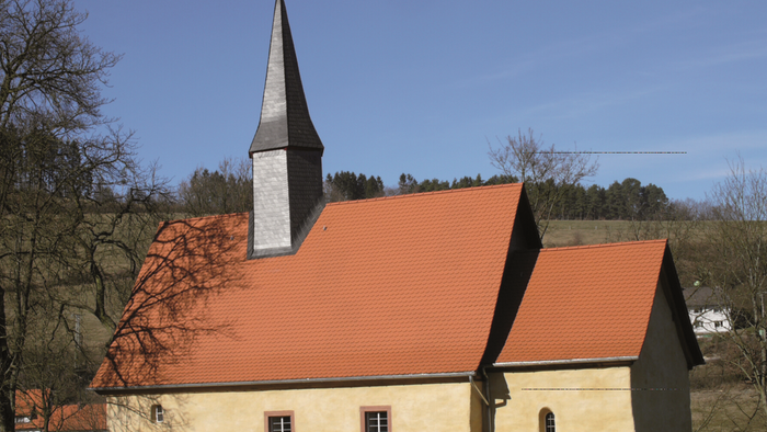 Kleine Kirche mit hohem Turm und rotem Dach in ländlicher Umgebung
