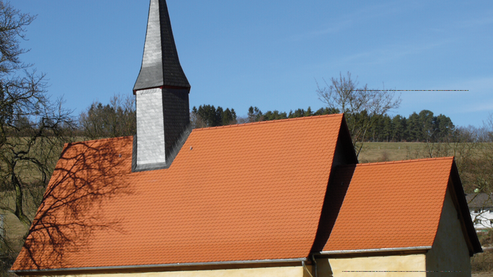 Kleine Kirche mit hohem Turm und rotem Dach in ländlicher Umgebung