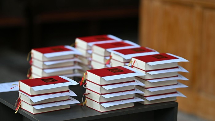 Aufgestapelte Bücher mit roten Einbänden und orangefarbenen Lesebändern, ordentlich auf einem Tisch im Freien arrangiert.