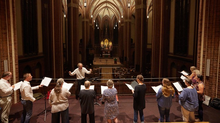 Chorprobe in einer prächtigen Kathedrale, wobei der Dirigent von vorne leitet.