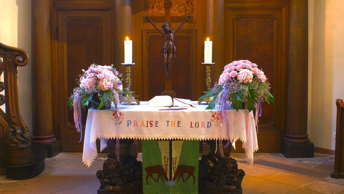Kirchenaltar mit Kruzifix, Kerzen, Blumen und einem Banner mit der Aufschrift *„Lobt den Herrn“*