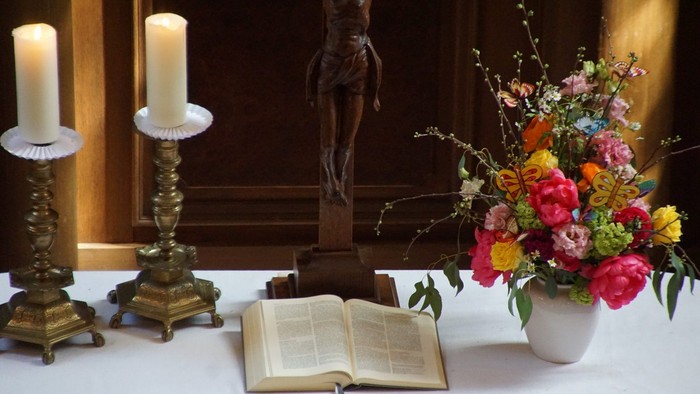 Kerzen, Kruzifix, aufgeschlagenes Buch und Blumen auf dem Tisch